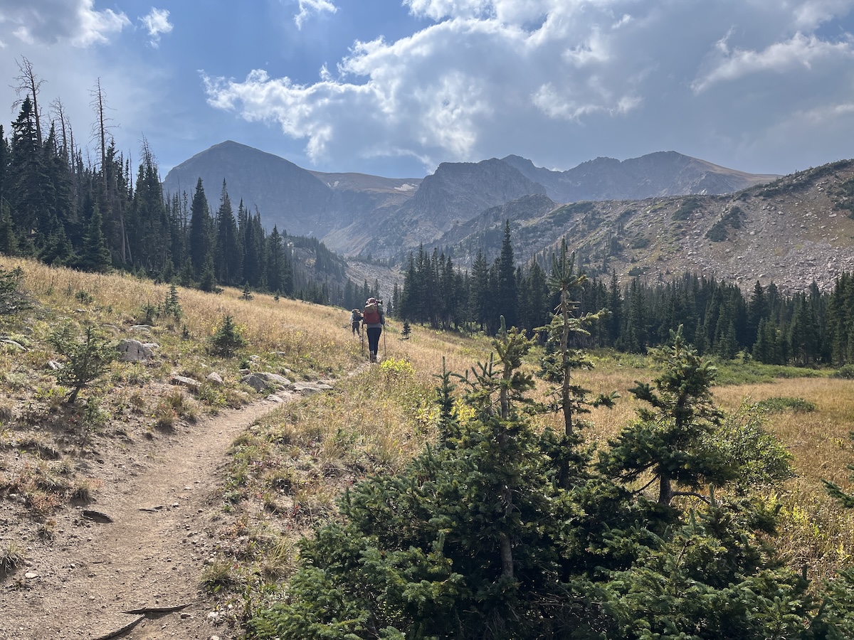 Wide open valley with mountains in the background and hikers on the trail in the foreground